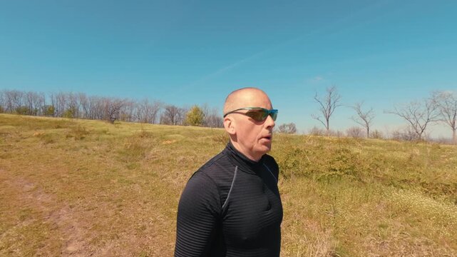 Close up shot of a mature man in his 50s running in nature. Focus on his face, sunglasses, and emotions during an active outdoor jogging session on a sunny day.
