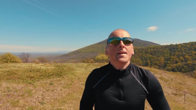 Close up shot of a mature man in his 50s running in nature. Focus on his face, sunglasses, and emotions during an active outdoor jogging session on a sunny day.