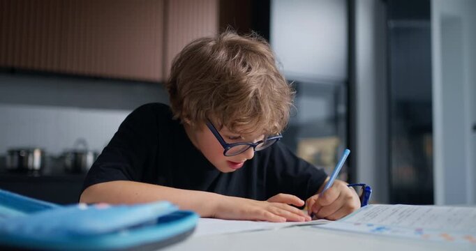 Young Boy Concentrating While Writing At Table. Determined Young Boy Practices Writing With Steady Effort