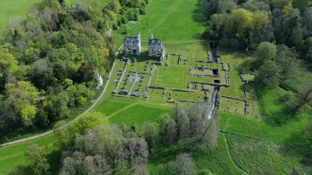 High angle aerial drone view of ancient abbey ruins in a lush green valley countryside landscape in the United Kingdom