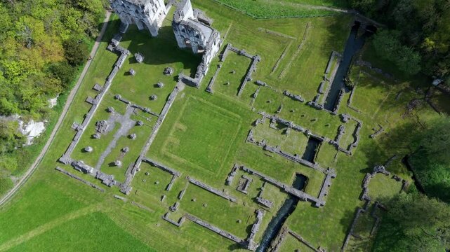 High angle aerial drone view of ancient abbey ruins in a lush green valley countryside landscape in the United Kingdom