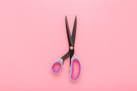 New dark black dressmaker scissors for fabric cutting on light pink table background. Pastel color. Closeup. Top down view.
