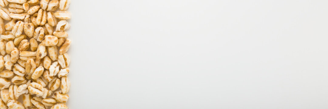 Yellow dry puffed wheat flakes on light gray table background. Closeup. Wide banner. Empty place for text. Top down view.