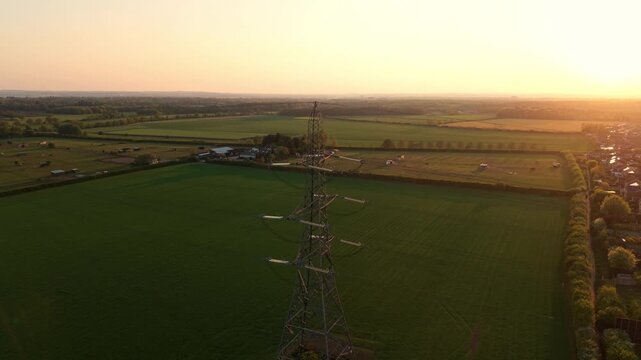 High angle aerial drone view close up of a steel lattice high voltage electricity pylon overlooking rural agricultural fields during a golden hour sunset near Doncaster UK