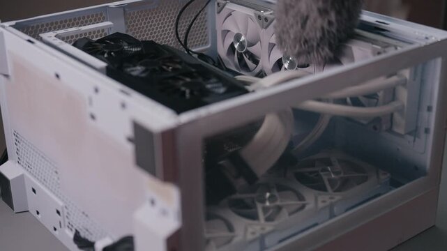 Professional technician using duster to clean internal components of desktop computer, removing accumulated dust from fans and graphics card for hardware maintenance, close-up, slow motion.