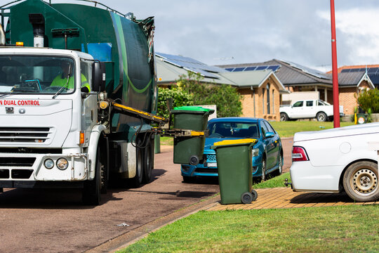Streetscape scene of garbage truck emptying green fogo bin on urban street