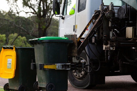 Streetscape scene of garbage truck emptying green fogo bin on urban street