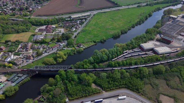 Freight train crossing a rail bridge near a large industrial manufacturing area, aerial view, Ferrybridge, UK.