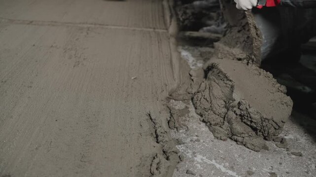 Close up of worker applying fresh cement mortar to floor. Builder uses trowel to level concrete screed during renovation. Construction and home improvement concept