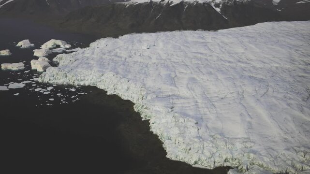 Aerial Greenland icecap meeting fjord, fractured glacier tongue flowing into dark water, scattered icebergs and broken sea ice, overcast light, remote scale