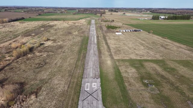 Cinematic drone shot flying forward along the weathered asphalt of decommissioned runway 09 at Markham Airport, showing the large closure 'X' mark
