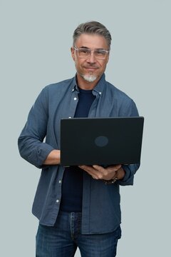 Casual mid adult man standing holding laptop computer. Portrait of happy middle aged male in 50s with gray hair and glasses, smiling. Isolated on white background.