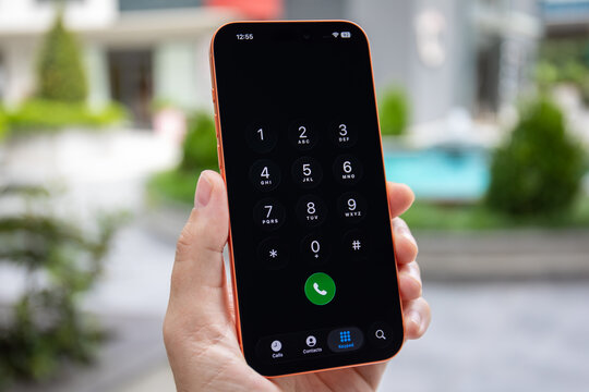 Man hand holding Phone Apple iPhone 17 Pro Max Cosmic Orange outdoor, displaying phone dialer keypad with numbers and green call button on the screen IOS 26