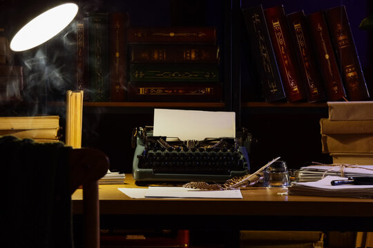 Author's workplace with vintage typewriter and glowing lamp near bookshelf in dark office