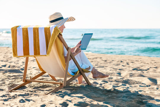 Woman using tablet while relaxing on beach chair by the sea