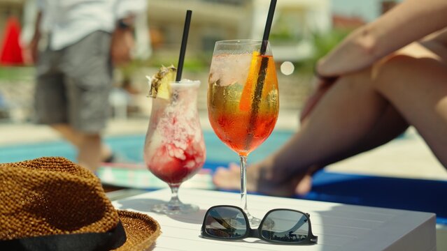 Cold colorful cocktails standing on table by pool on hot sunny summer day. Couple enjoying vacation in tropical luxury hotel resort garden. Careful relaxing lifestyle on holiday trip.