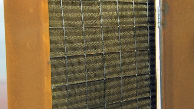 A gleaming, pristine ventilation filter is carefully guided into its robust, rust-toned metal housing. Observe the intricate grid and mesh preparing to purify the air within an industrial setting.