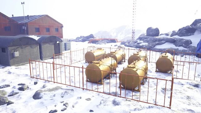 Snowcovered fuel tanks inside fenced compound, orange maintenance huts and containers, icy ground with gravel patches, industrial piping and valves, bright