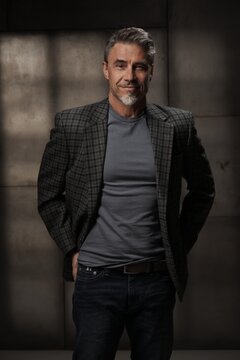 Casual mid adult man standing. Portrait of happy middle aged male entrepreneur in 50s with gray hair, smiling. Confident businessman in business casual on gray background.