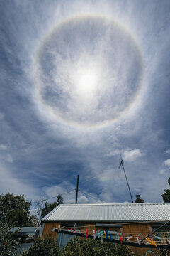 Sun halo optical phenomenon in a cloudy sky above a suburban rooftop