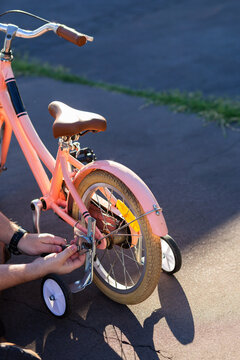 dad fixing training wheels on child&rsquo;s bike while sitting on driveway