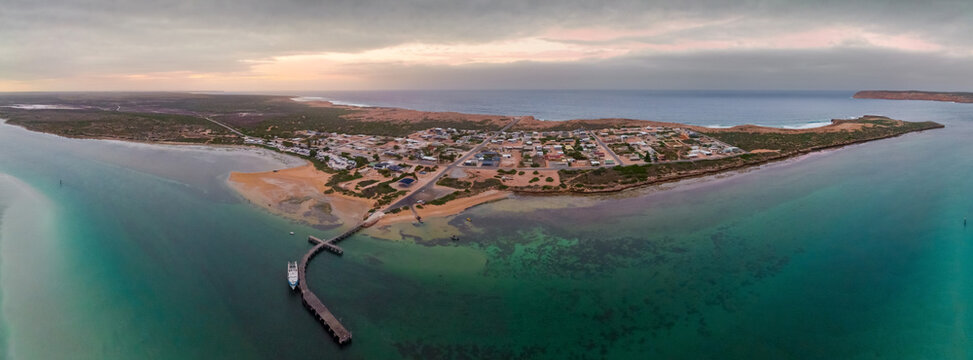 Aerial panorama view of a small coastal town and jetty on a peninsula under a subdued dawn sky