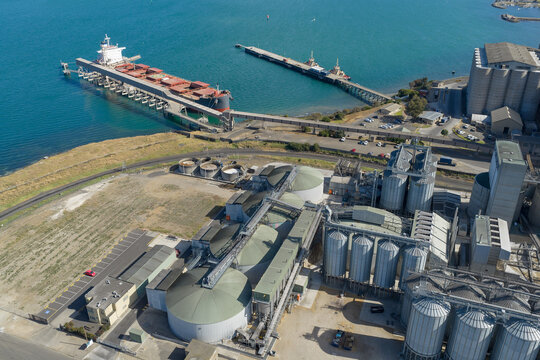 Aerial view of a cargo ship at a port with storage tanks and silos