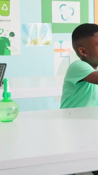 Vertical video: Reaching student in green tee lifting seed tray by laptop studying fern for lesson