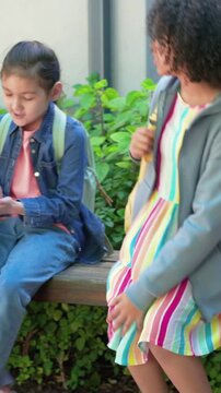 Entering corridor student with yellow backpack joining denim jacket peer on bench playing hand game