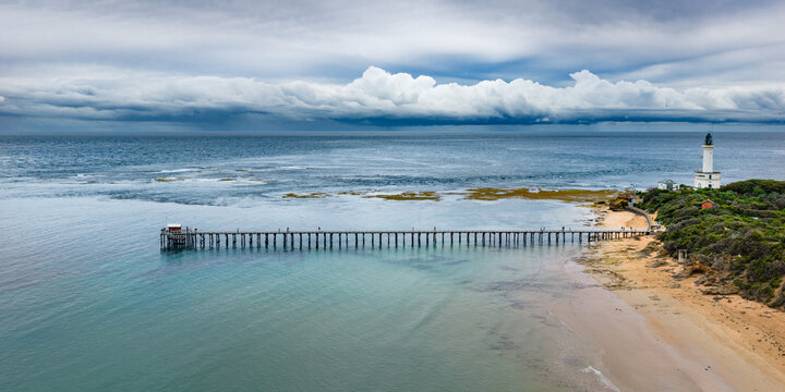 Aerial view of storm clouds approaching a coastal lighthouse and long narrow jetty over a calm bay