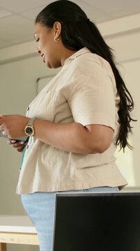 Vertical video: Looking down at phone, presenter giving briefing in classroom, in beige blouse