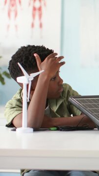 Vertical video: Noticing tilted solar panel pupil in green tee at lab lifting hand studying turbine