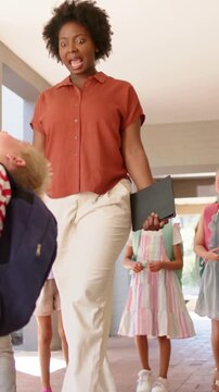 Vertical video: Walking lady in rust top with folio watching kids in hall as blue pack boy passing