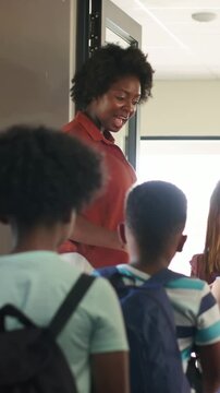 Vertical video: Opening door, teacher in rust blouse guiding backpacked children into classroom