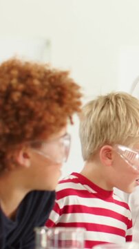 Vertical video: Pair leaning, watching demo starting in lab in goggles, eyeing green beaker striped
