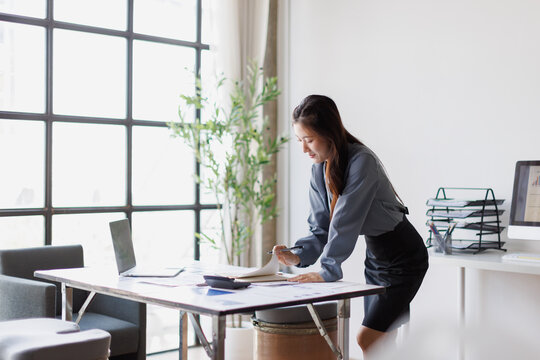 Businesswoman standing at desk reviewing documents in modern office