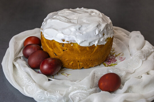 Orthodox Easter Kulich Cake with Red Eggs on Floral Plate Draped with White Lace Cloth