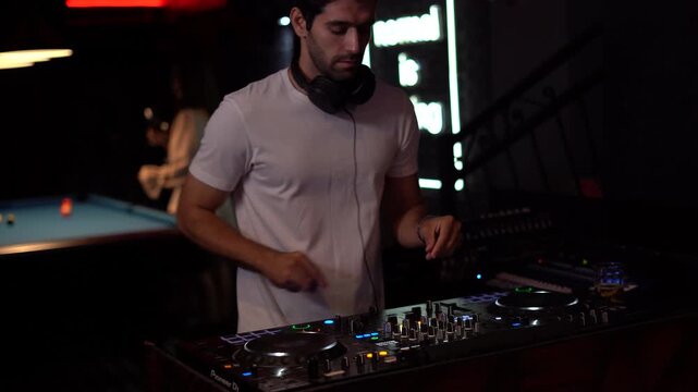 Professional man DJ mixing music on a controller and wearing headphones in a nightclub. Disc jockey performing at a party in a bar with neon lights. Nightlife and entertainment.