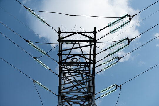 High voltage power line tower against blue sky with clouds, illustrating electricity transmission, energy infrastructure, and modern technology.
