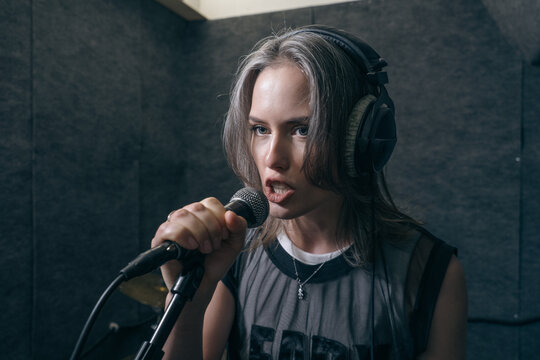 Female singer with headphones singing into microphone in rehearsal studio.