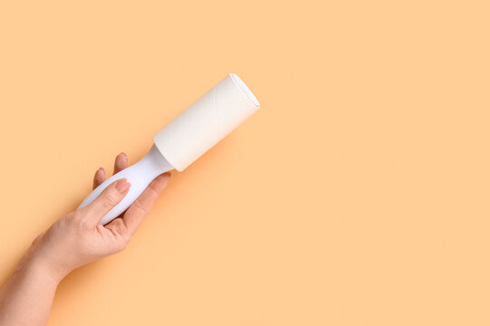 Female hand with lint roller on beige background