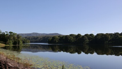 Fototapeta premium Serene Lake Reflection with Lush Green Forest and Distant Mountains