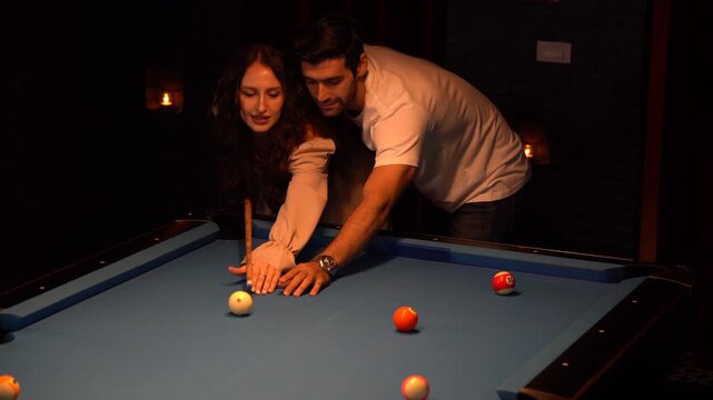 Affectionate young man and woman sharing a romantic moment while playing billiards at a bar. Beautiful couple dating and laughing together in a nightclub. Nightlife and intimacy.