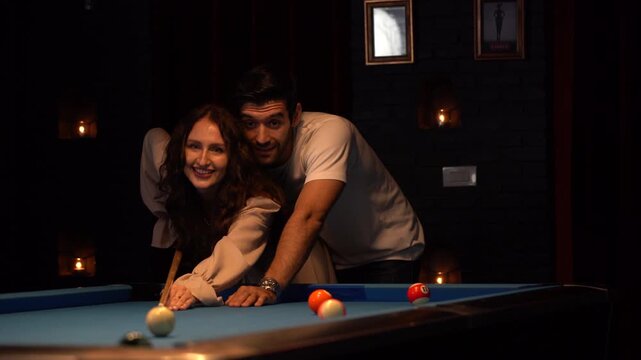 Affectionate young man and woman sharing a romantic moment while playing billiards at a bar. Beautiful couple dating and laughing together in a nightclub. Nightlife and intimacy.