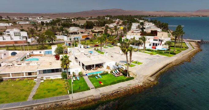 Aerial of coastal homes and palm trees along Paracas waterfront in Peru beside Pacific Ocean, establish