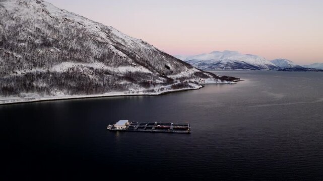Polar night arcing aerial view of aquiculture cod farm in snowy fjord