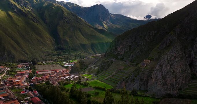 Historic town and ancient Inca ruins of Ollantaytambo nestled in deep valley of Andes mountains, Peru. Aerial forward