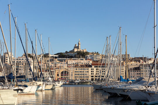 Basilique Notre-Dame de la Garde sur la colline au centre de l'image, vue de face depuis le quai du Vieux-Port, bateaux &agrave; quai formant une perspective vers la Bonne M&egrave;re, ciel bleu, ville de Marseille