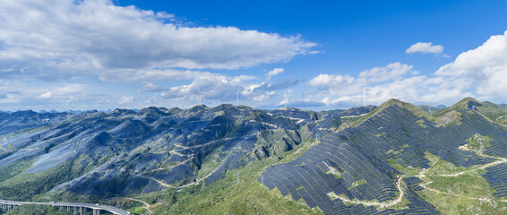 Panoramic View of Integrated Renewable Energy Landscape with Solar Terraces and Wind Turbines on Mountain Ridges