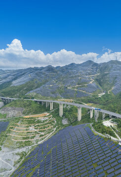 Highway Traverses Expansive Solar Farms and Wind Turbines Spanning Mountainous Terrain